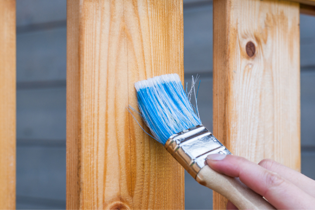 Fence staining by worker with brush and stain.