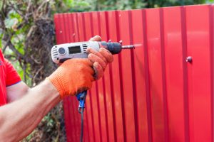 Metal Fence being installed by worker with power tool.